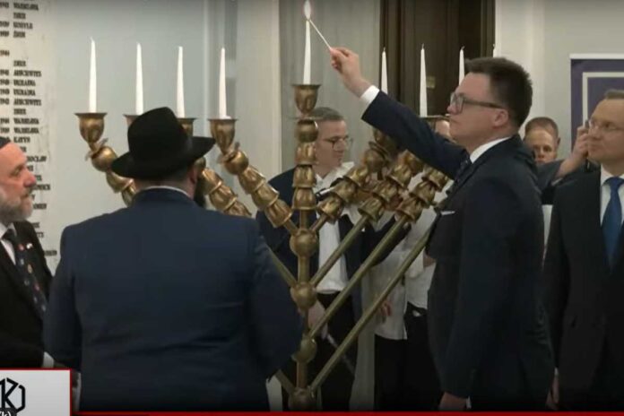 Marszałek Sejmu RP Szymon Hołownia odpala świecę chanukową na chanukii, spoglądając w stronę rabinów. Po prawej stronie Prezydent RP Andrzej Duda