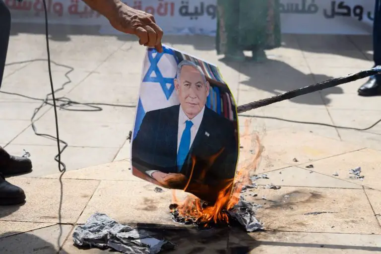 Protestujący palą zdjęcie Benjamina Netanjahu.