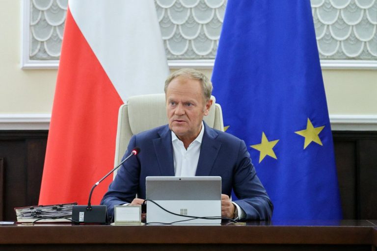 Donald Tusk na tle flag Polski i Unii Europejskiej.