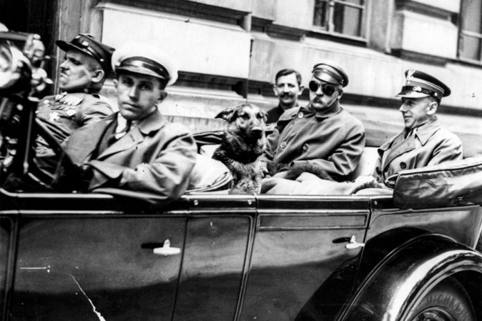 NCZAS.INFO | Zdjęcie ilustracyjne. Wyjazd Józefa Piłsudskiego z Warszawy do Sulejówka 1929/07/11 Na tylnym siedzeniu samochodu siedzą Józef Piłsudski (po lewej stronie, w goglach), mjr Konrad Zembrzuski (z prawej) i pies 